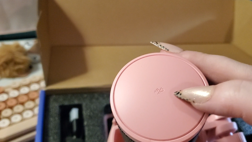 a close up of the top of the pink fifine microphone. heyshadylady's fingers, with long pointed fingernails, are pointing out the symbol on the top of the mic which is a microphone with a slash through it, indicating this is a mute button.